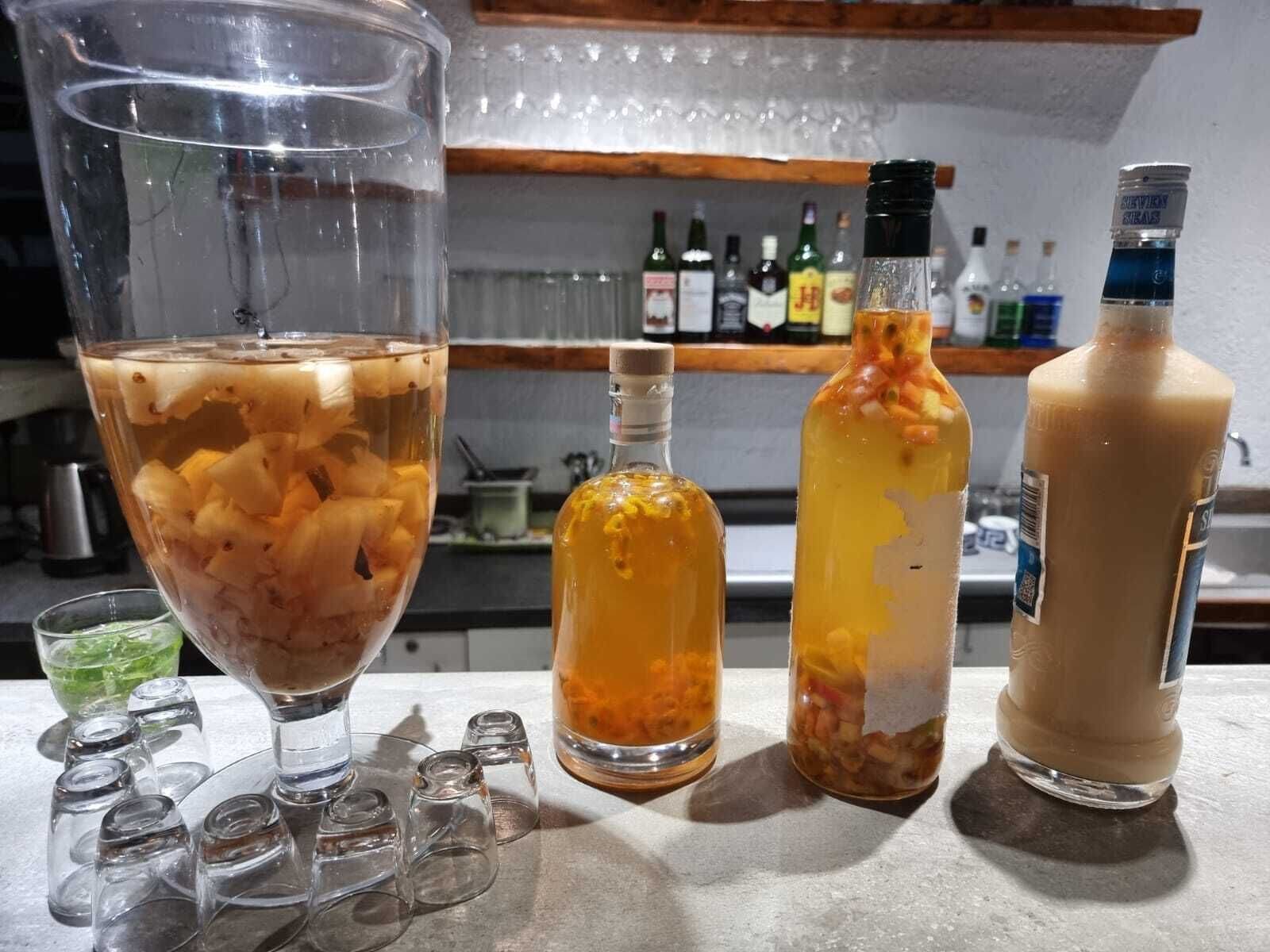 Una zona de bar con un vaso grande que contiene una bebida con hielo y fruta, dos botellas con etiquetas y una botella de salsa.