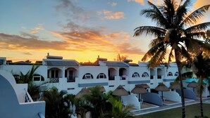 Un resort con edificios blancos, sombrillas de paja y palmeras.