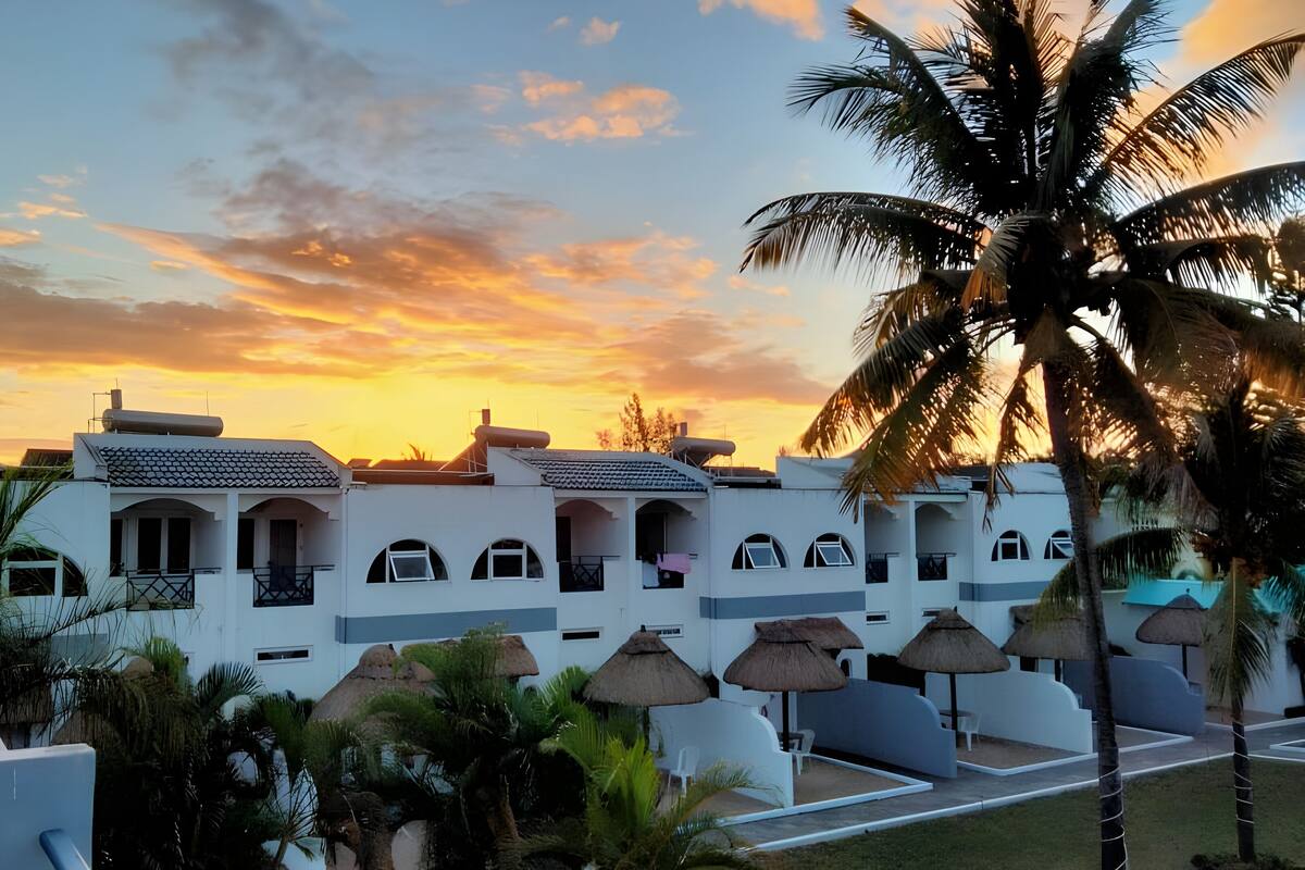 A resort with white buildings, thatched umbrellas, and palm trees.