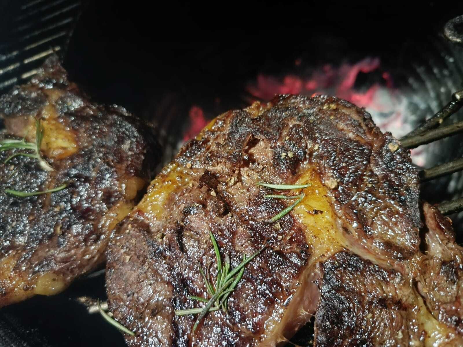 Carne a la parrilla con marcas visibles de carbonización y ramitas de romero, indicando una actividad de cocina o asado.