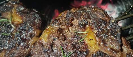 Carne a la parrilla con marcas visibles de carbonización y ramitas de romero, indicando una actividad de cocina o asado.
