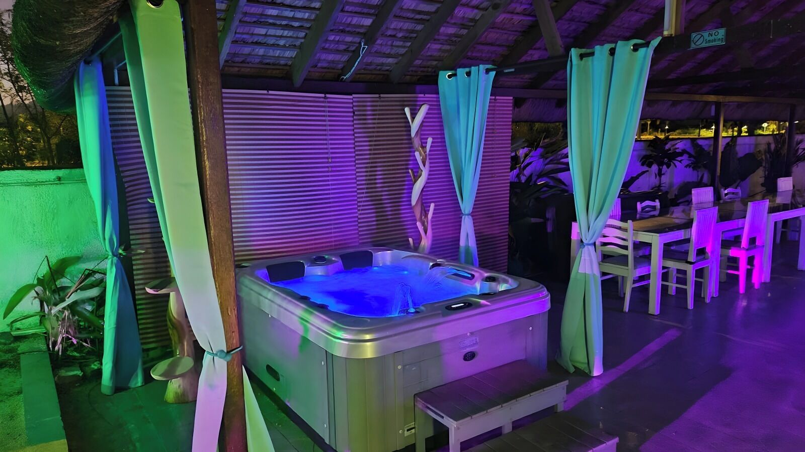 A hot tub with a metallic finish, surrounded by green curtains and a wooden structure.