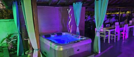 Un jacuzzi con acabado metálico, rodeado de cortinas verdes y una estructura de madera.
