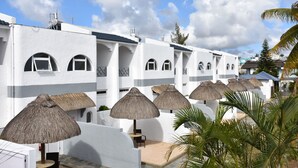 Una hilera de edificios blancos con ventanas arqueadas y sombrillas de paja.