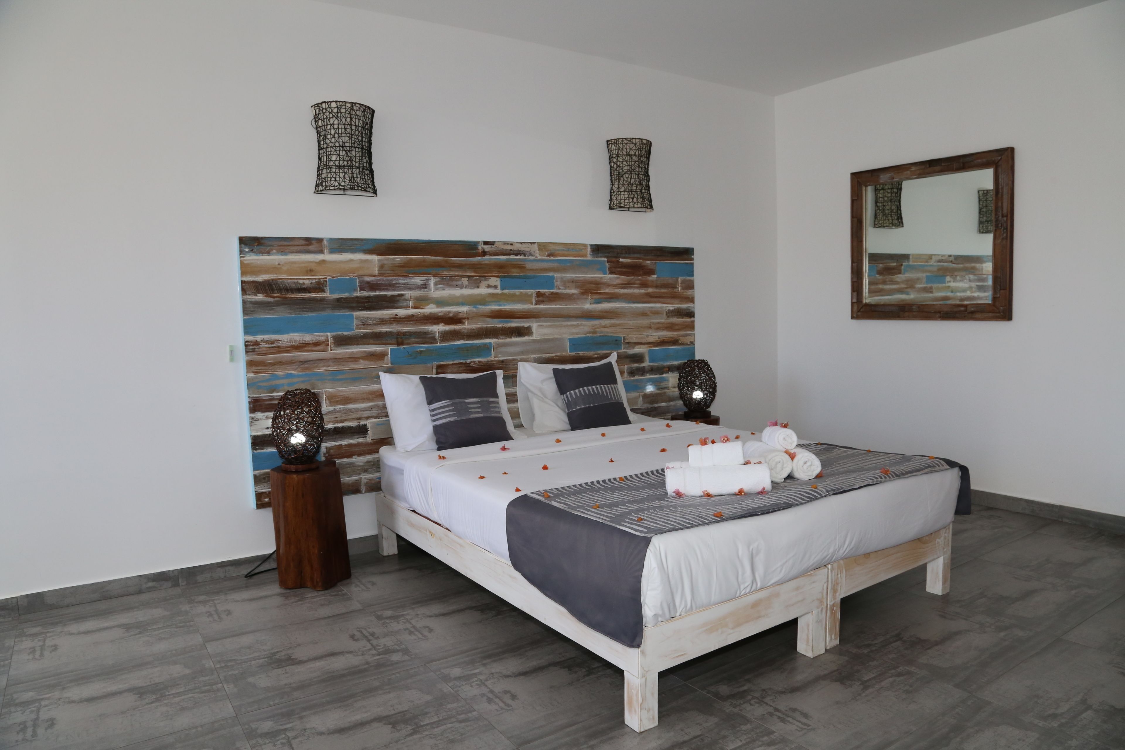 A bedroom with a wooden headboard, a bed with white bedding, two bedside tables, and a mirror on the wall.