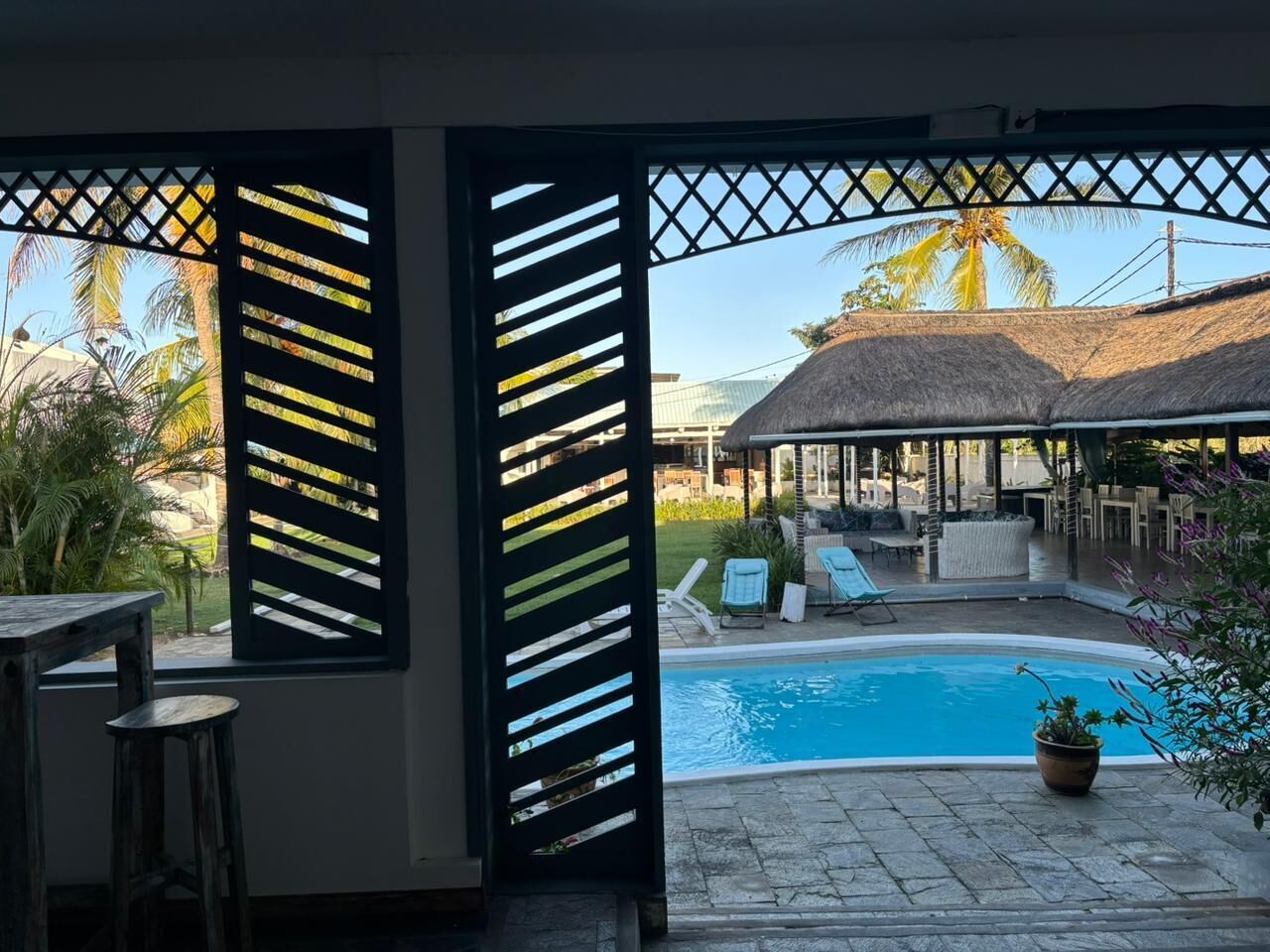 A pool area with lounge chairs, a thatched-roof structure, and a view of palm trees.