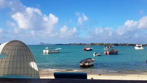 Escena costera con barcos amarrados en un puerto deportivo, cielo despejado y una montaña distante.