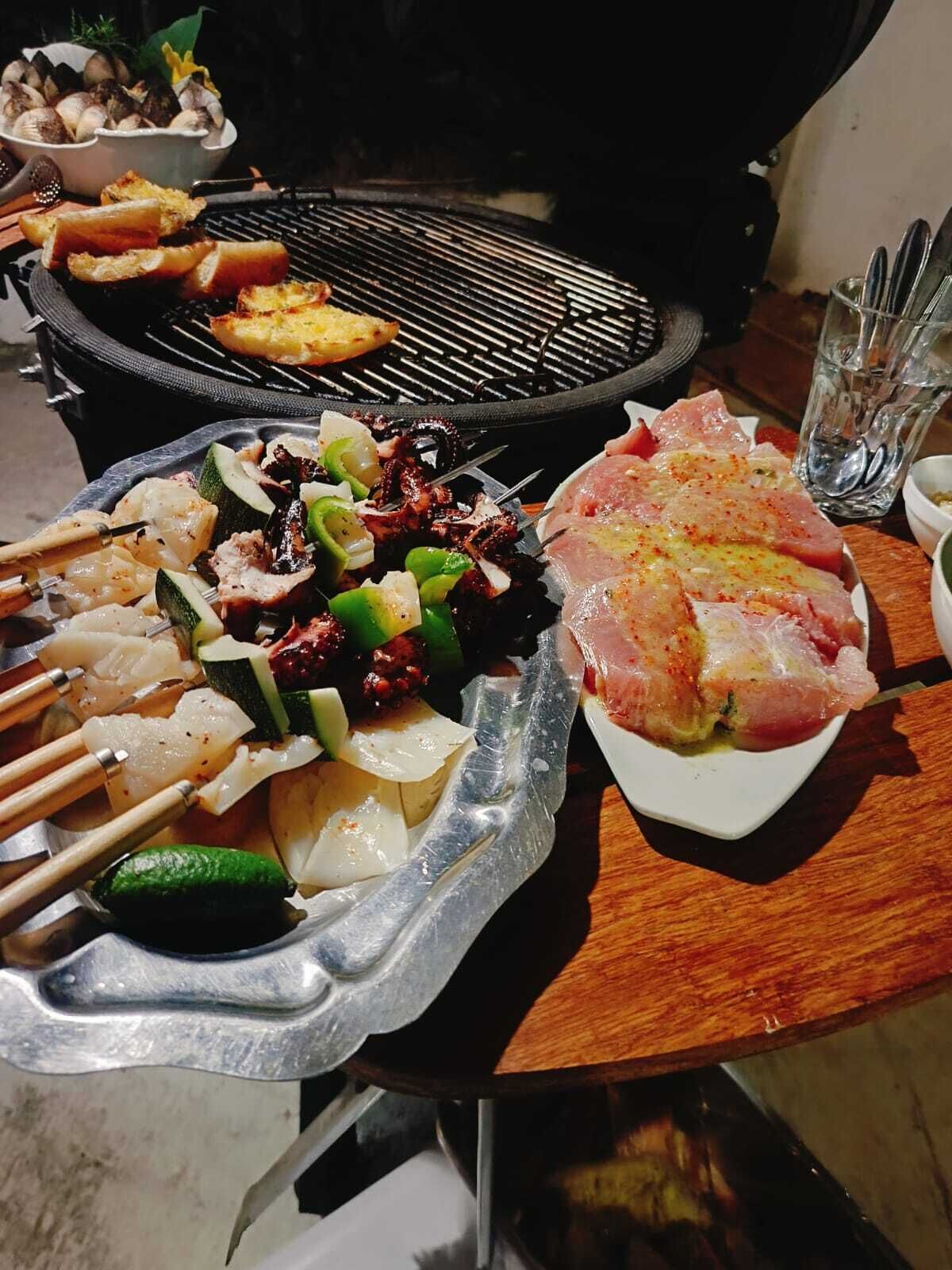 Una parrilla con brochetas de mariscos y vegetales, un tazón de hongos y un plato de carne cruda.