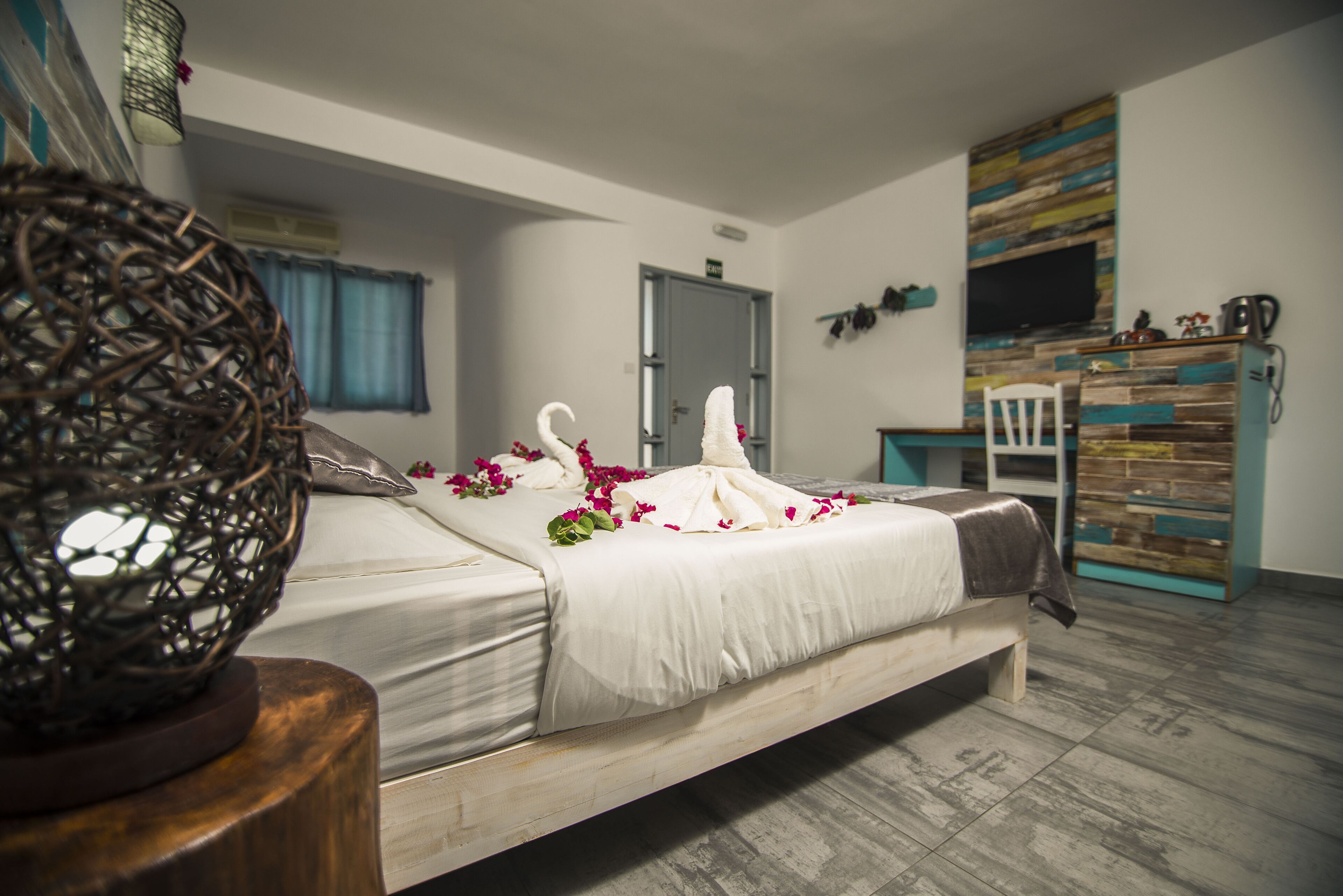 A bedroom with a bed, a wooden floor, a door, a TV, and a small table.