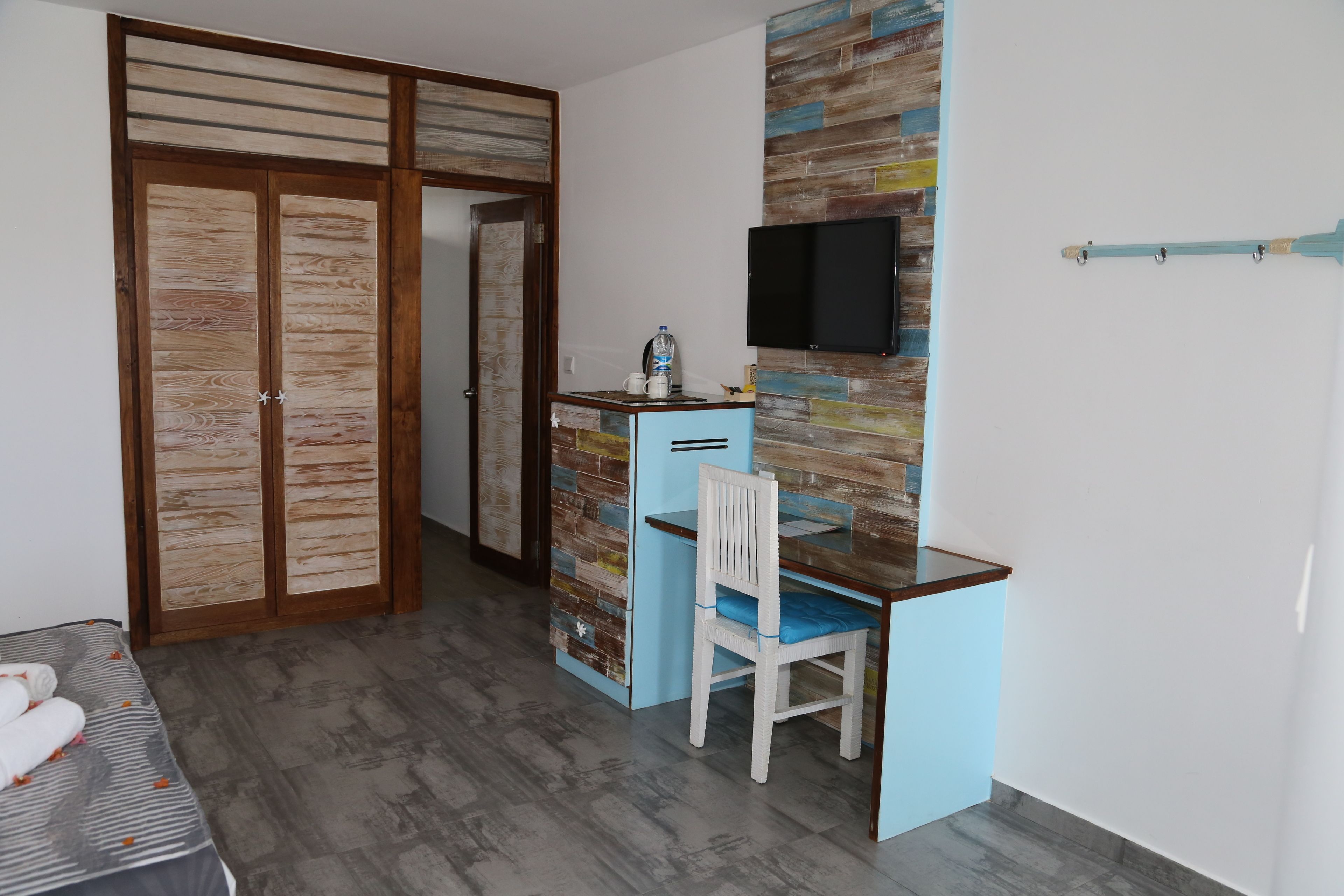 A room with a desk, chair, wardrobe, and a mounted TV.