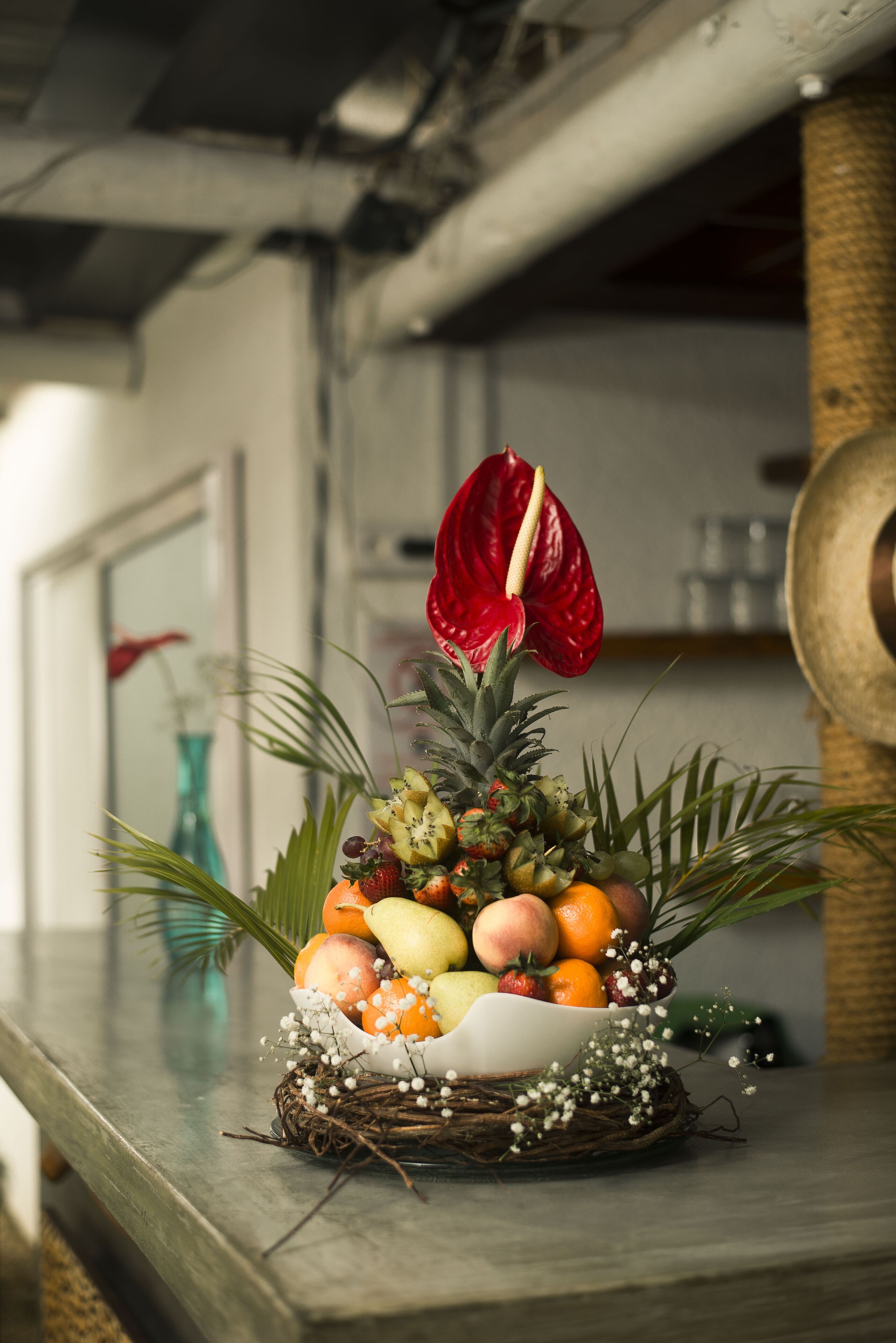 A fruit arrangement on a wooden surface with a red flower, surrounded by a nest-like structure.