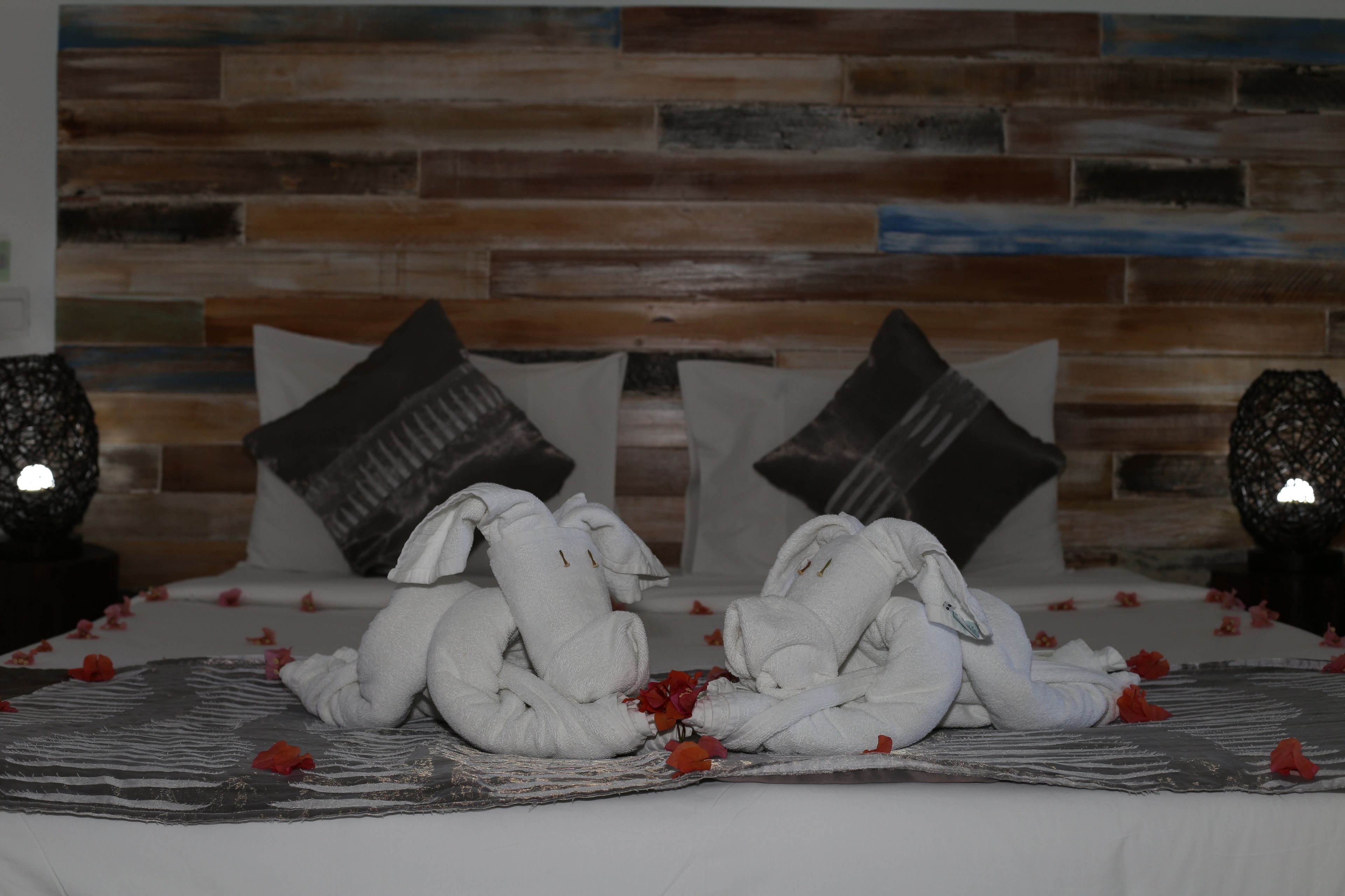 Un lit avec des serviettes disposées de manière décorative, un mur en bois avec un motif en briques et deux coussins décoratifs.