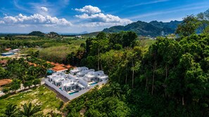 Un hotel moderno con varias construcciones, piscina y rodeado de exuberante vegetación y colinas.