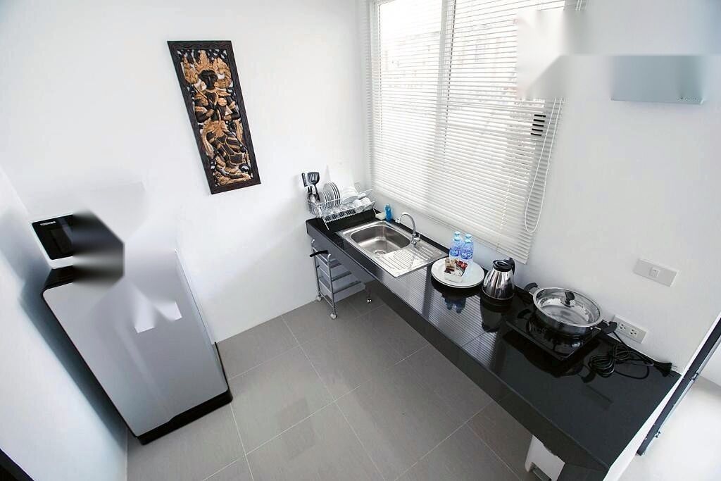 A compact kitchen with a black countertop, a sink, a kettle, and a window with blinds.