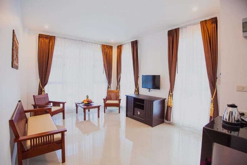 A modern living room with a flat-screen TV, wooden furniture, and large windows with curtains.
