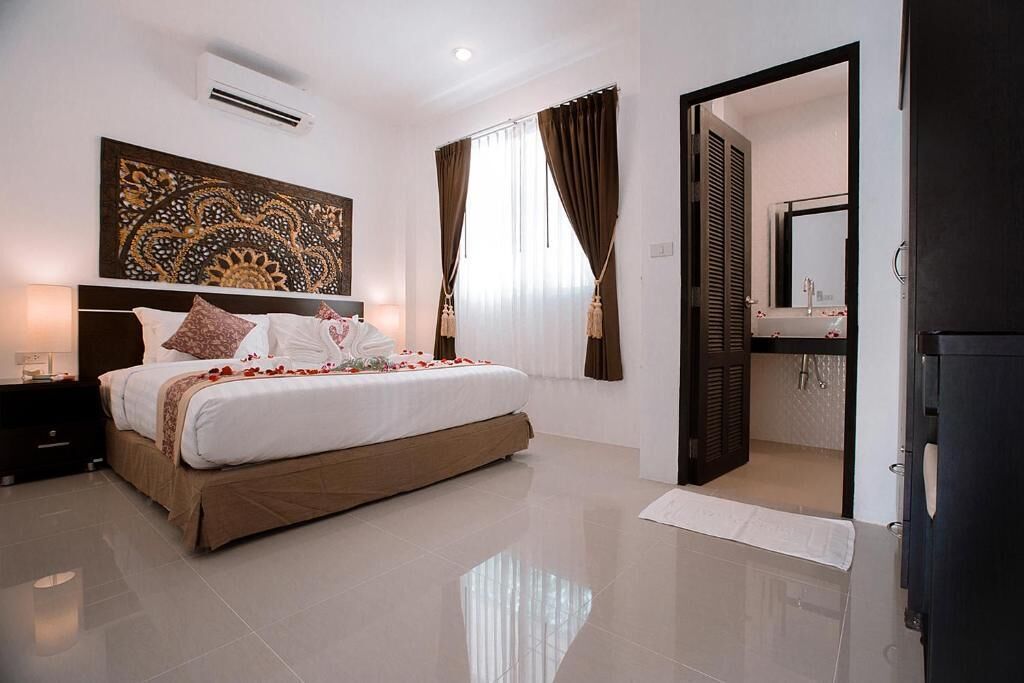 A modern hotel room with a large bed, a bedside table, a wall-mounted air conditioner, and a bathroom visible through an open door.