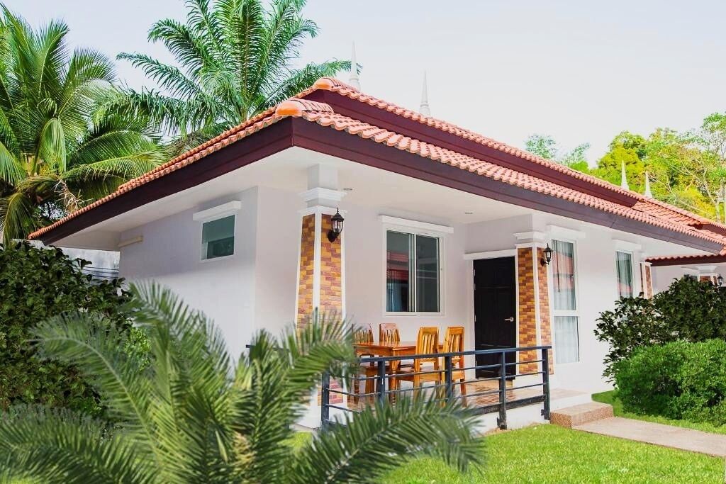 A single-story house with a tiled roof, a porch with a railing, and a small dining table with chairs.