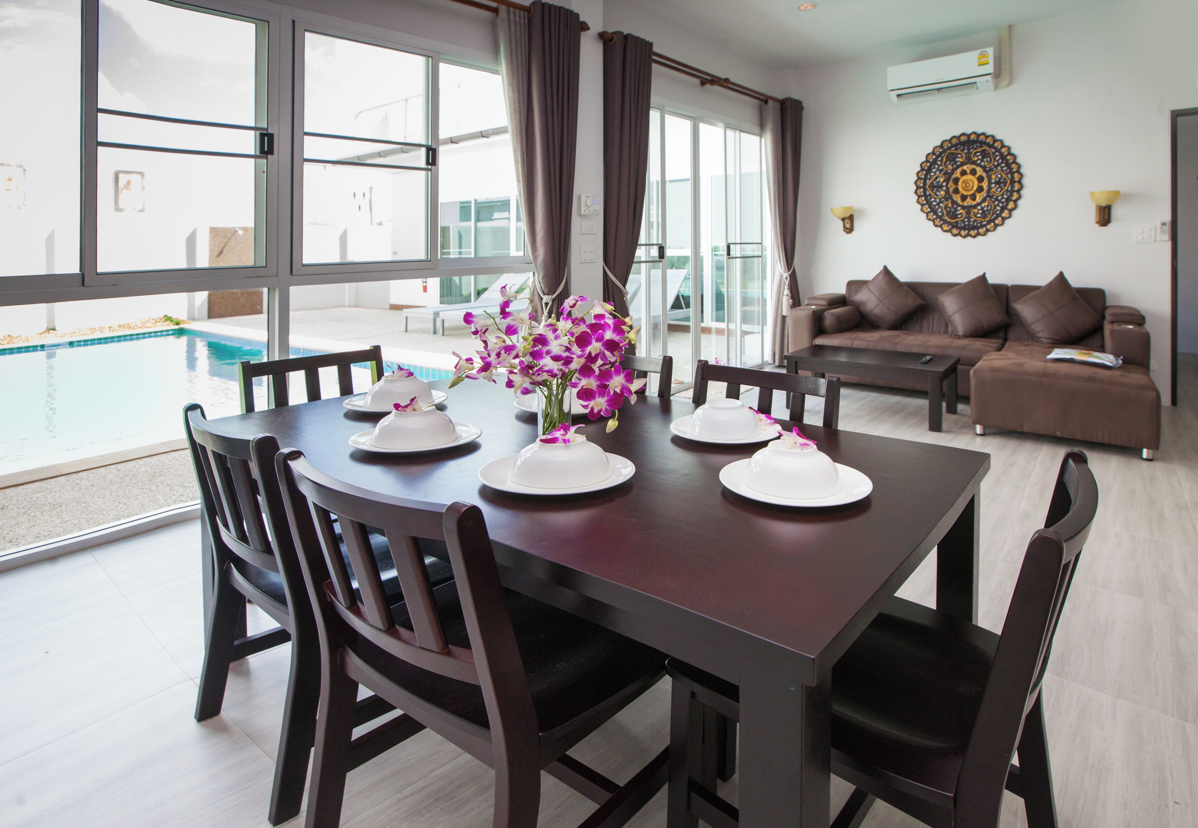 Un comedor con mesa preparada para cuatro personas, un sofá y vista a una piscina.