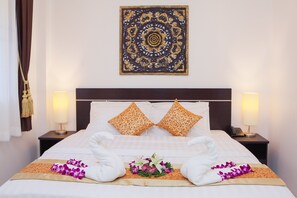Een netjes opgemaakt bed met twee kussens, een decoratieve wandversiering en een nachtkastje met een lamp.