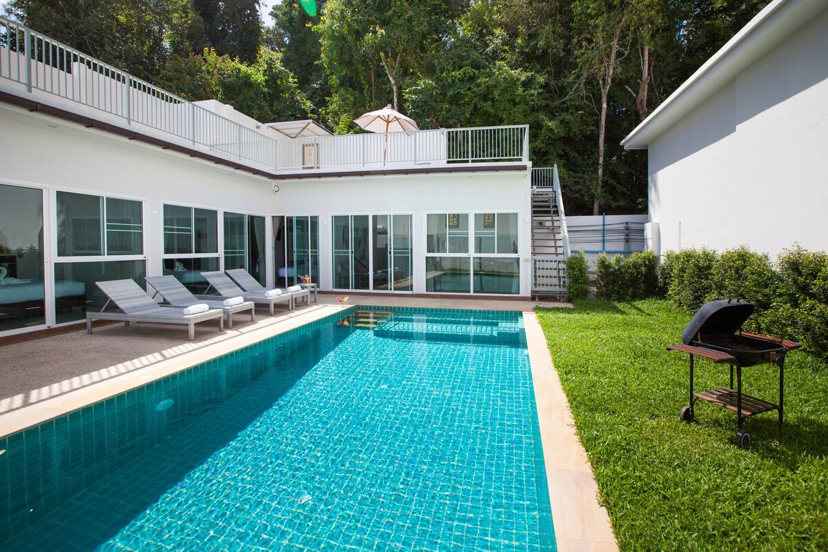 A modern house with a swimming pool, a barbecue, and a balcony.