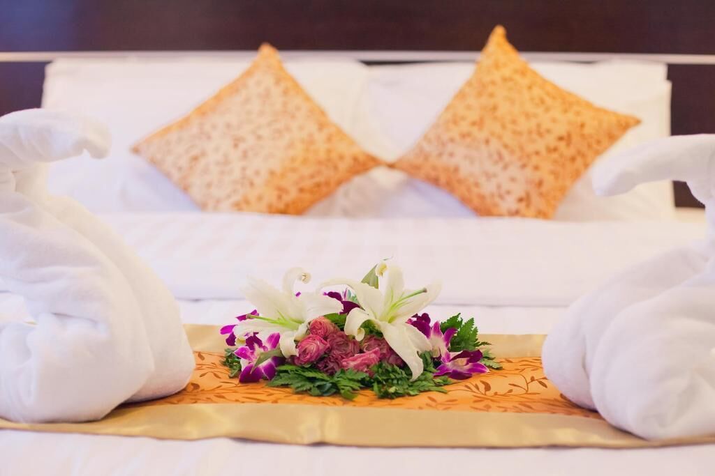 Un letto rifatto con cura e un'elegante composizione floreale al centro, affiancata da asciugamani.