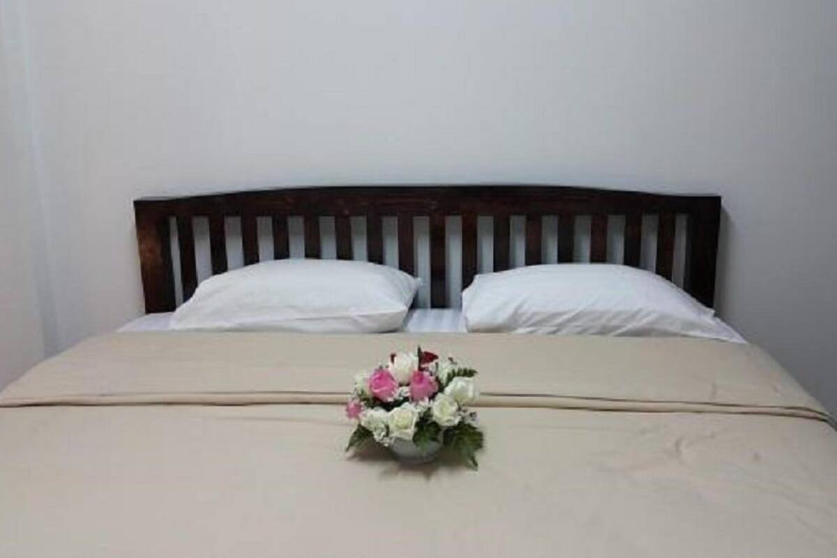 A bed with a wooden headboard, two white pillows, and a bouquet of flowers in a vase on the bed.