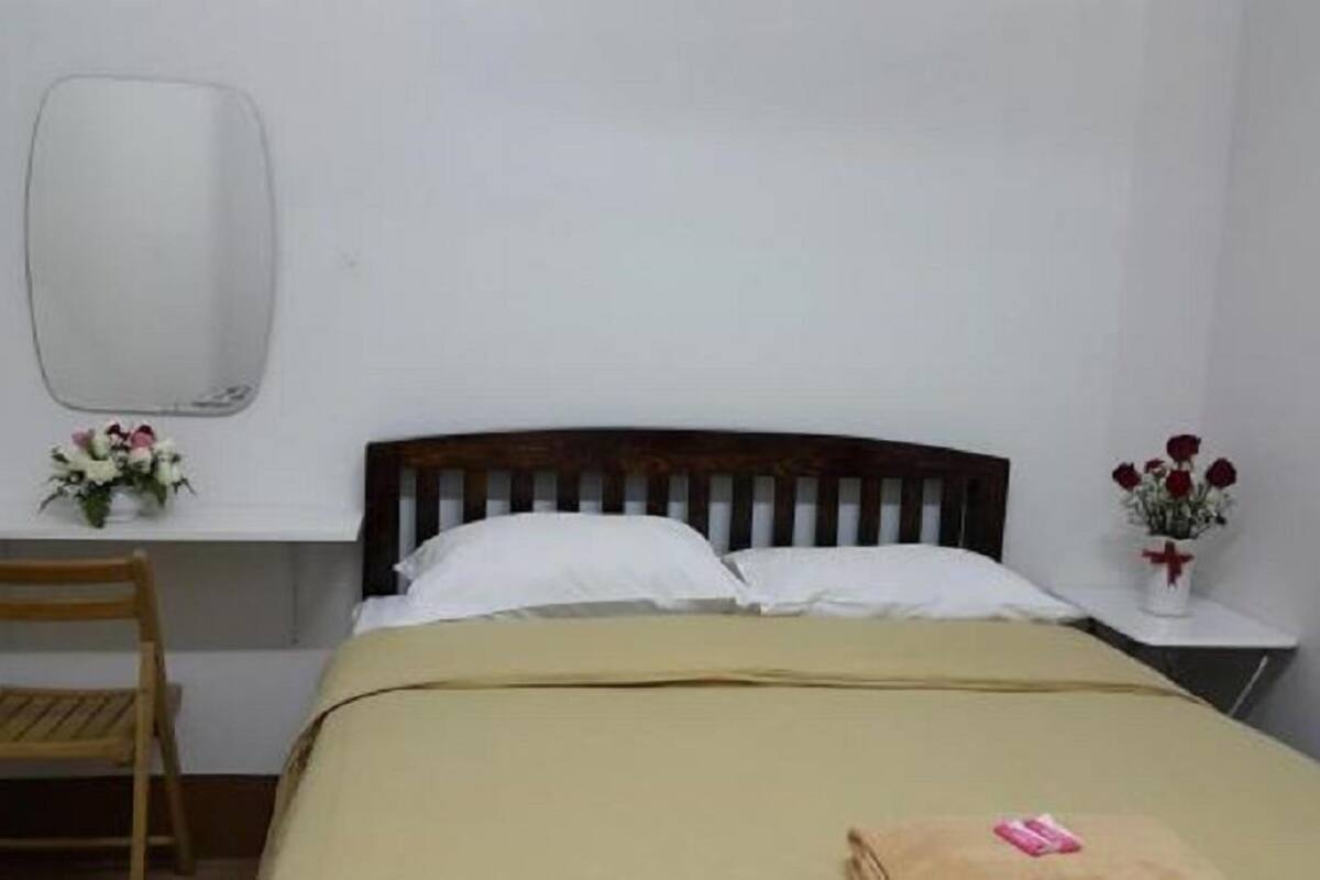 A simple room with a bed, a wooden chair, a desk, and a mirror.