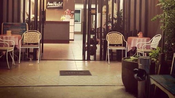 Un interior acogedor con una recepción que dice 'Ann Hostel', paredes a rayas, piso de baldosas y varias sillas y mesas.