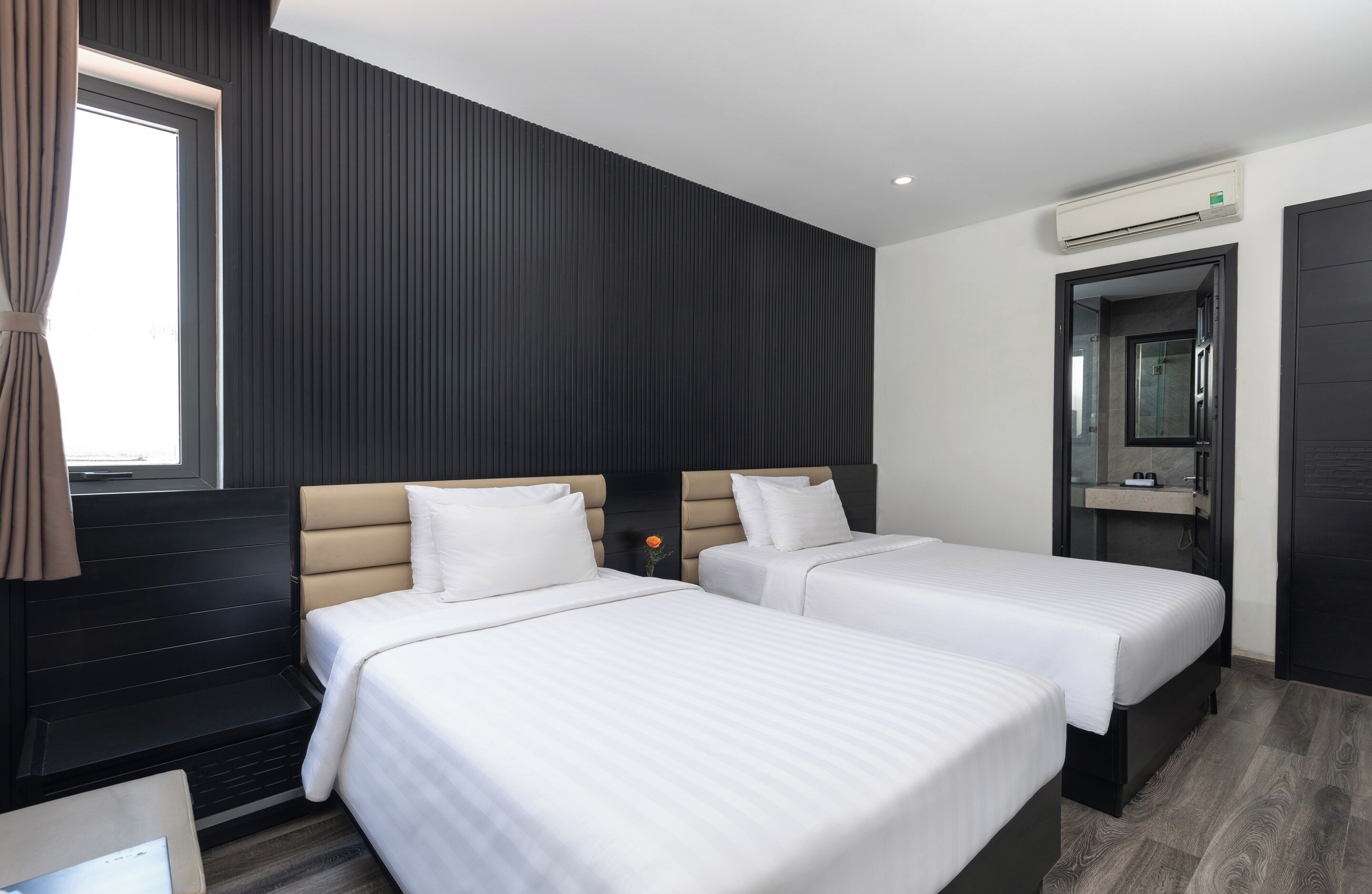 A hotel room with two beds, a window with curtains, a wall-mounted air conditioner, and a mirror.