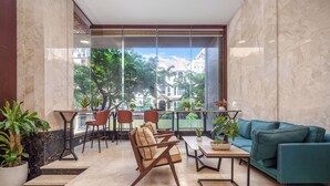 A modern lounge area with a sofa, chairs, and a table, featuring a large window with a view of buildings and trees. - Ocean Star Da Nang Bay Hotel (Da Nang)