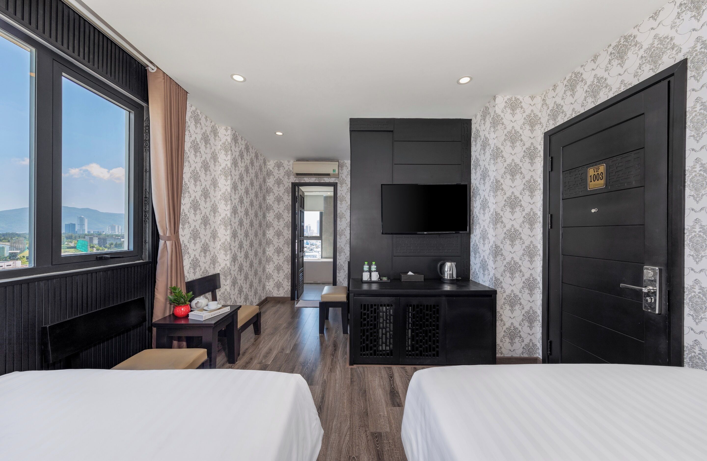Camera d'albergo con due letti, una TV, una scrivania con una macchina per il caffè e vista sulla città.