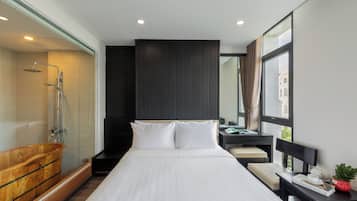 A modern hotel room with a large bed, a wooden bathtub, a glass-enclosed shower, and a view of a building through the window.