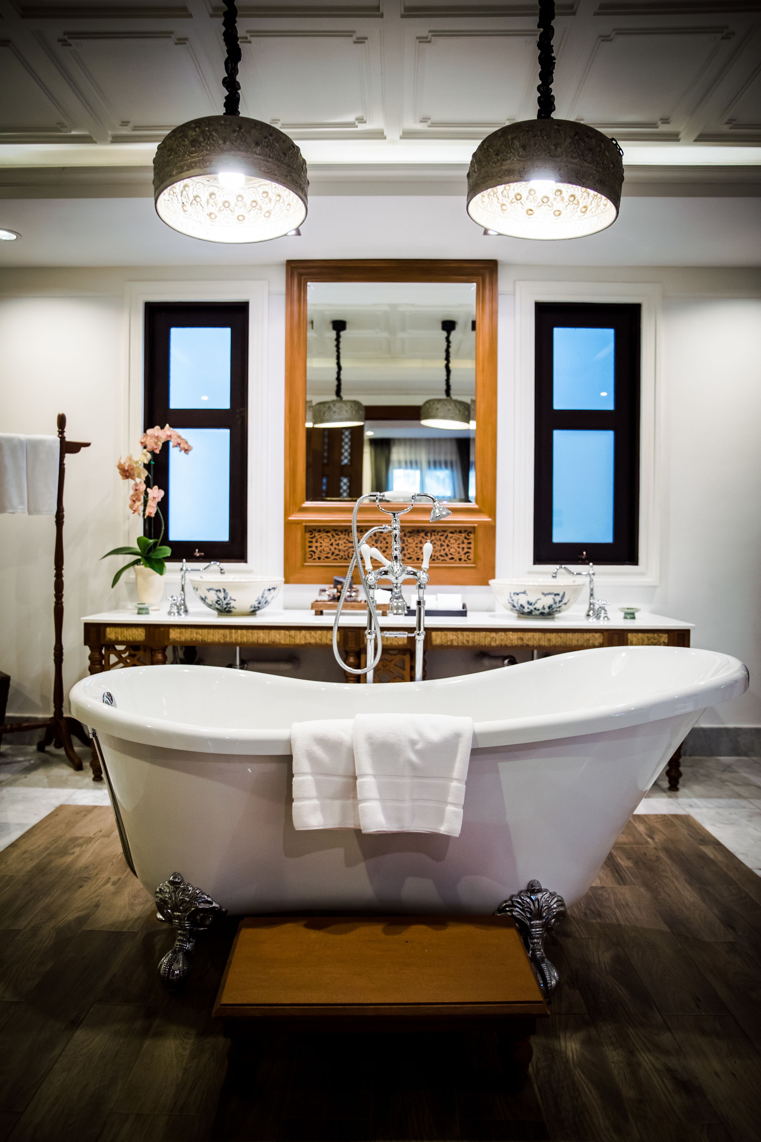 Une salle de bain avec une baignoire sur pieds, un meuble-lavabo en bois, un grand miroir et deux lampes suspendues.