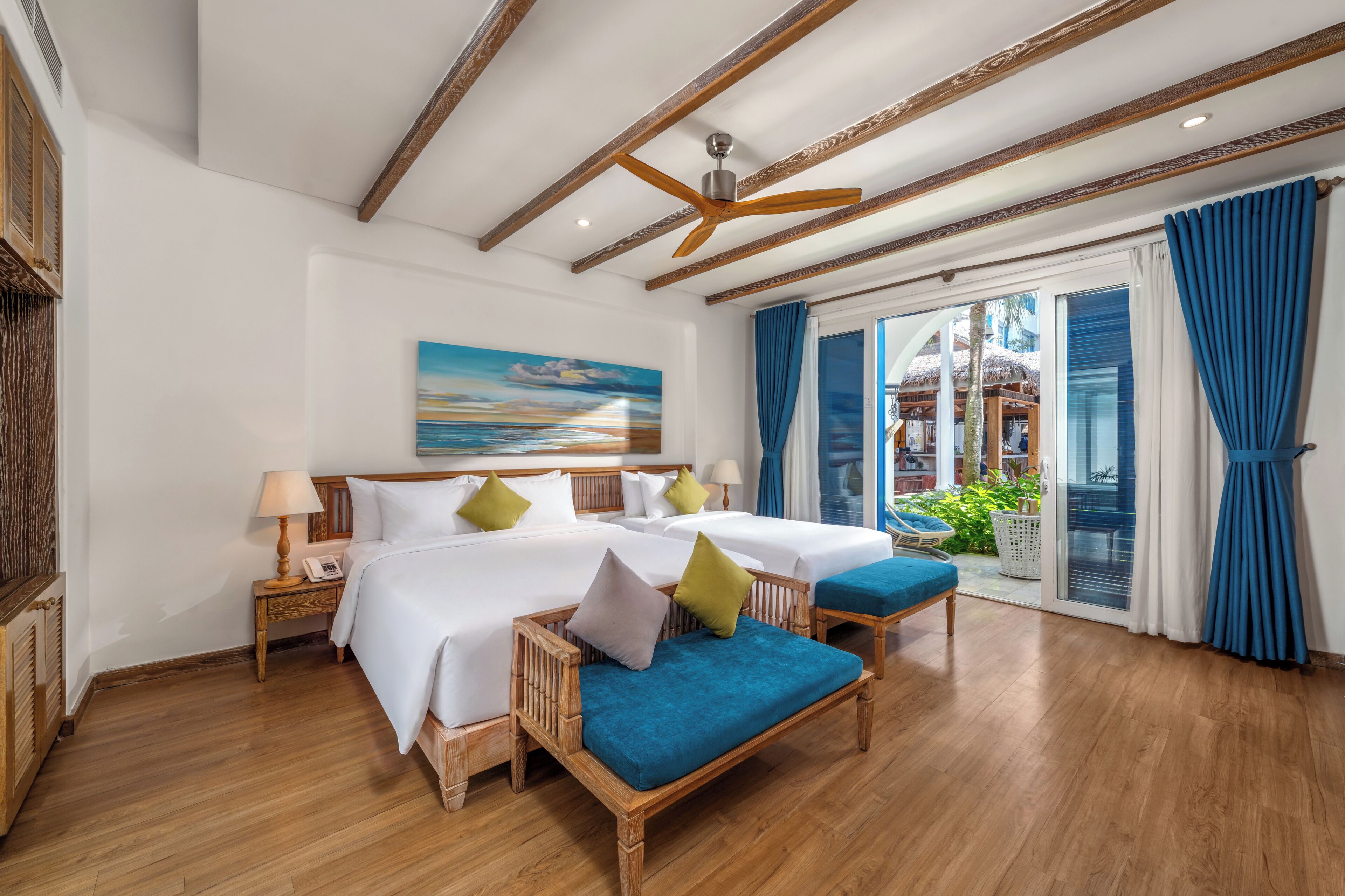 A hotel room with a large bed, two bedside tables, a ceiling fan, and a view of the outdoors.