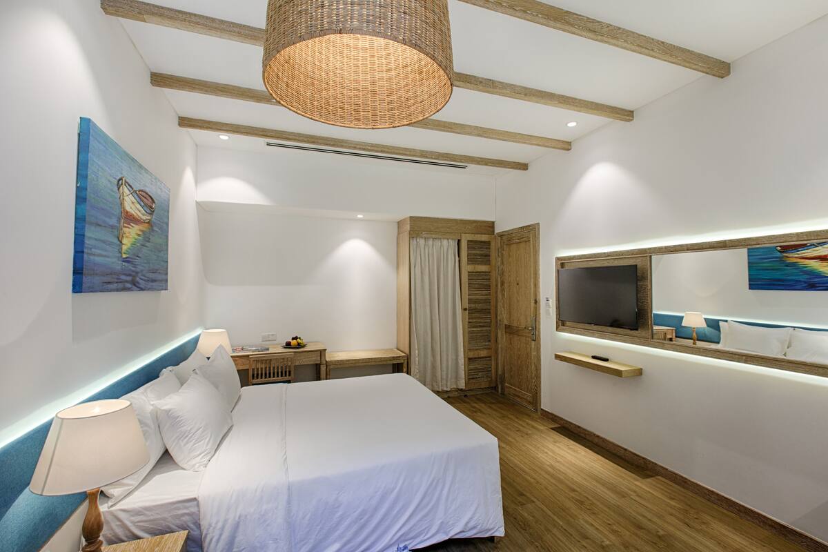A modern hotel room with a large bed, a TV, a wooden wardrobe, and a painting on the wall.