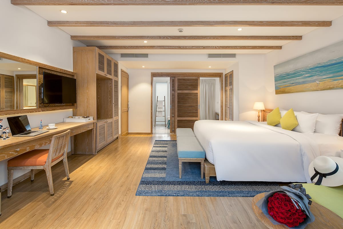 A hotel room with a wooden desk, a bed, a large mirror, and a painting of a beach scene.