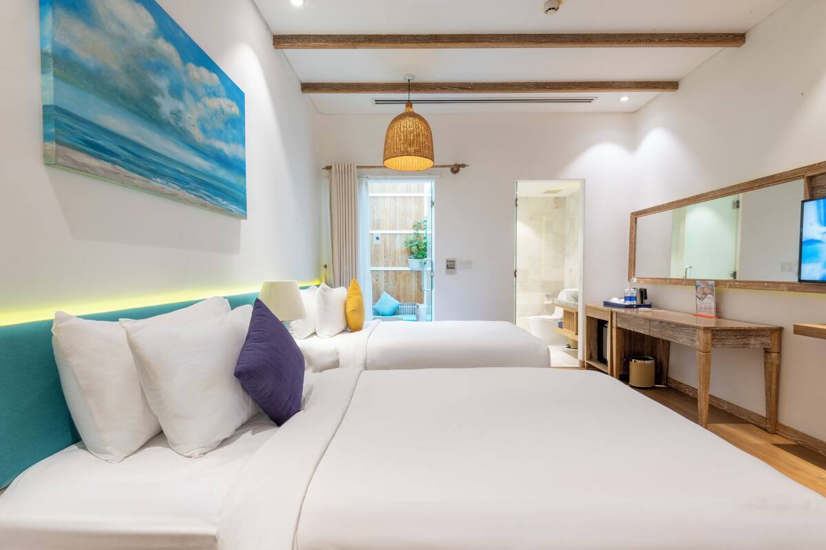 A modern hotel room with a large bed, a desk, a mirror, and a painting on the wall.