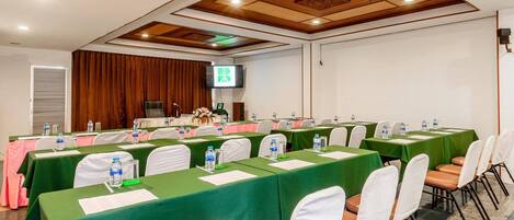 Un salón de conferencias con mesas verdes, sillas blancas y una pantalla de televisión.