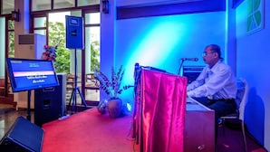 Ein Mann am Rednerpult mit Mikrofon, Computerbildschirm und Lautsprecher in einem Raum mit blauer Beleuchtung.