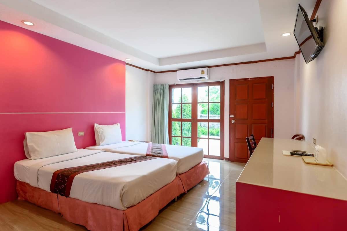Habitació d'hotel amb dos llits, un escriptori vermell, televisió i finestra amb vista a vegetació.