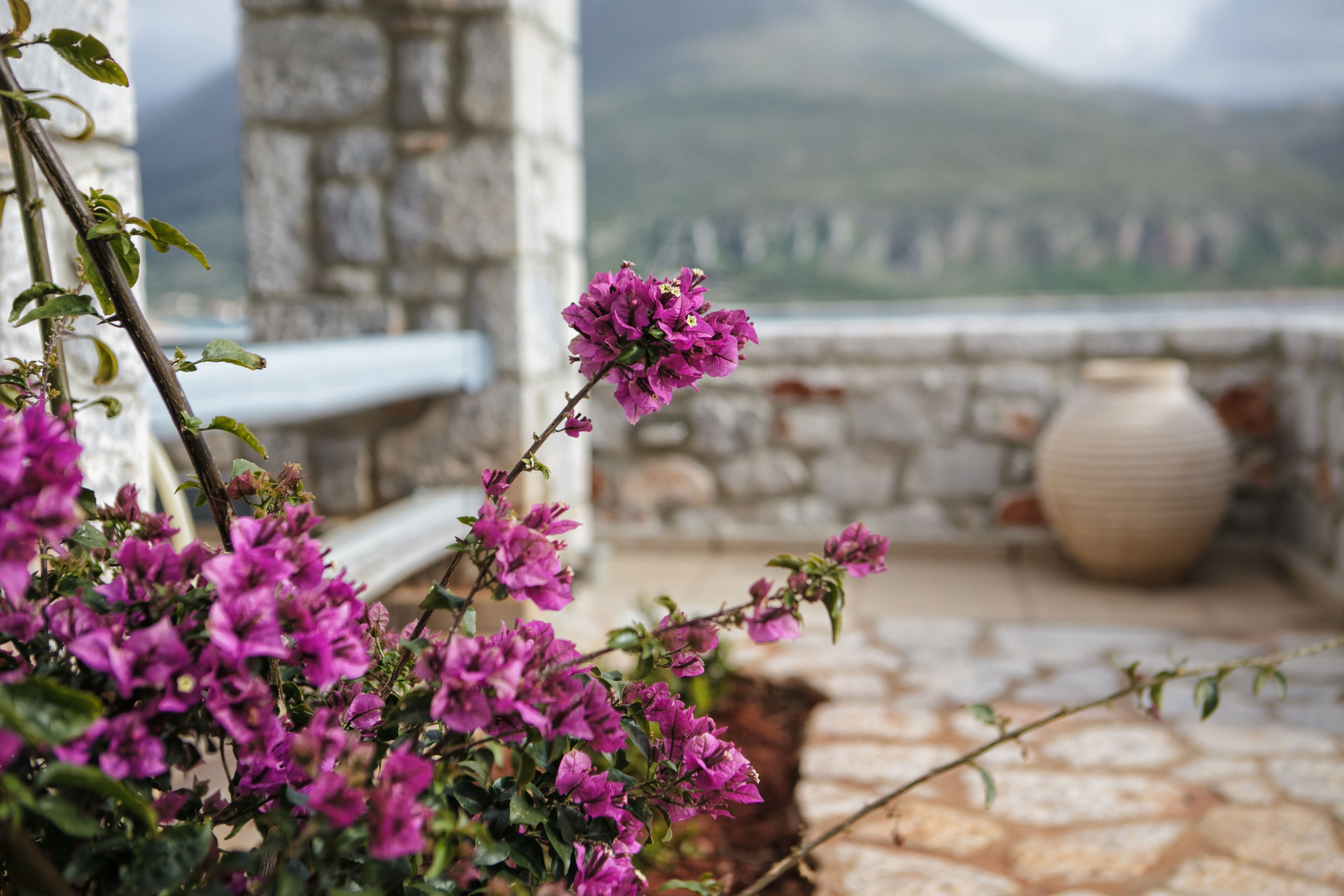 A balcony with a view of mountains, a stone wall, and a large vase.