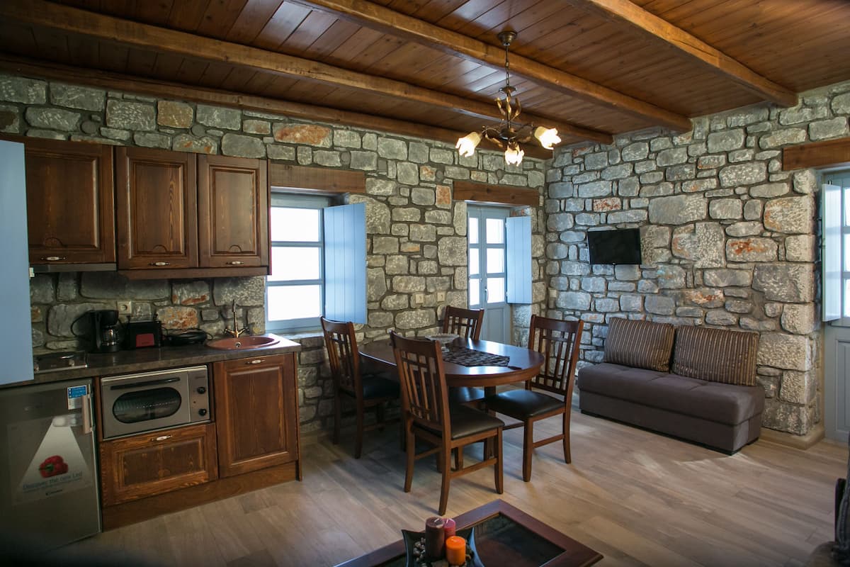 A stone-walled kitchen with wooden cabinets, a dining table with chairs, and a sofa.