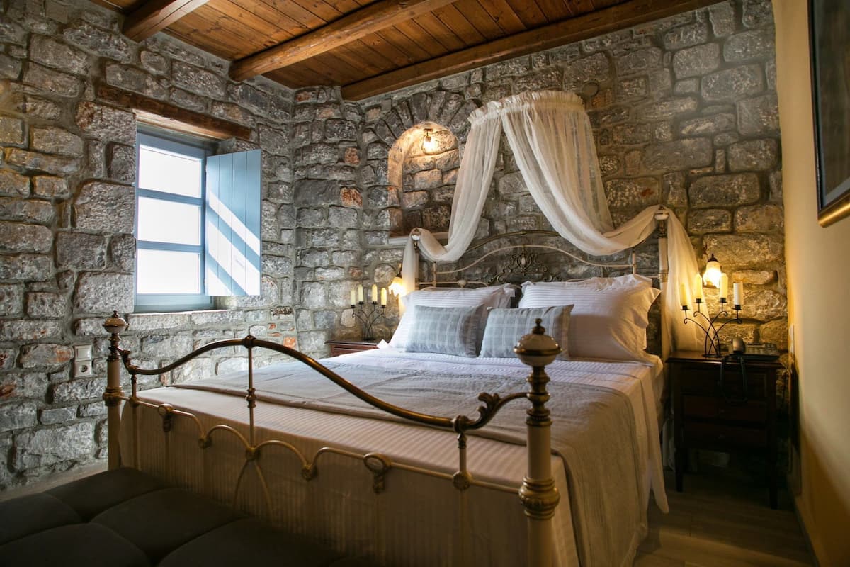 A stone-walled bedroom with a four-poster bed, a canopy, and a nightstand with candles.
