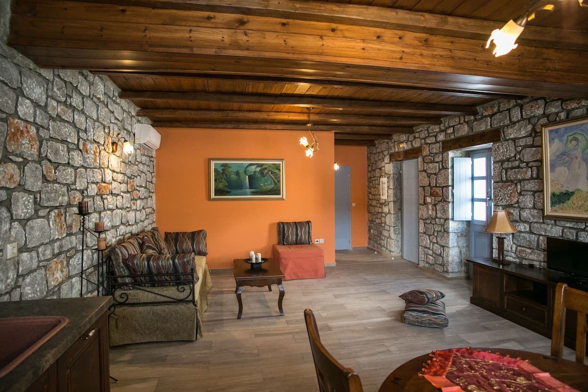 A cozy living room with stone walls, a wooden ceiling, a sofa, a coffee table, and a television.