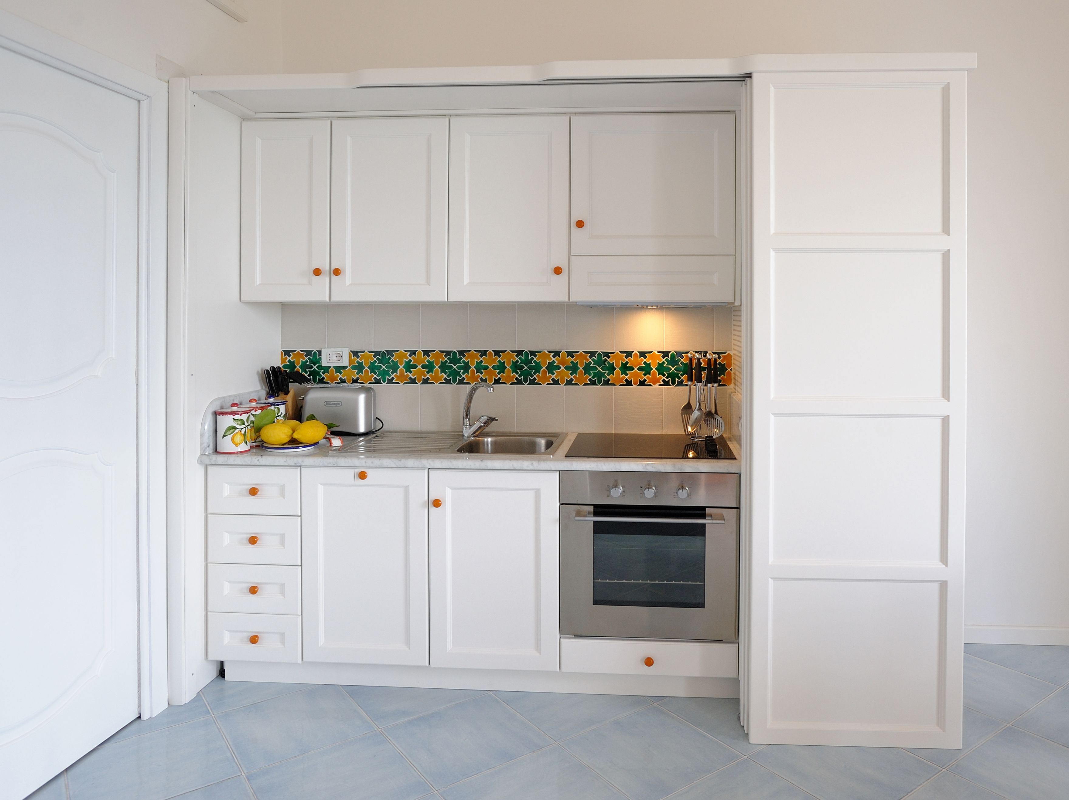 A compact kitchen with white cabinets, a stainless steel oven, and a colorful backsplash.