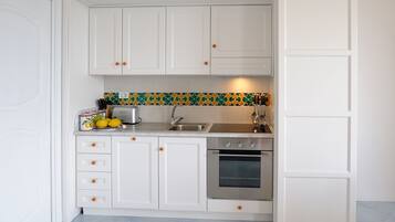 A compact kitchen with white cabinets, a stainless steel oven, and a colorful backsplash.