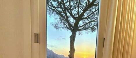 Una habitación con vista a un árbol y al atardecer sobre un paisaje costero.