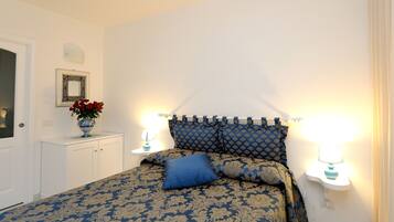 A bedroom with a bed, bedside lamps, a nightstand, a dresser, and a vase with flowers.
