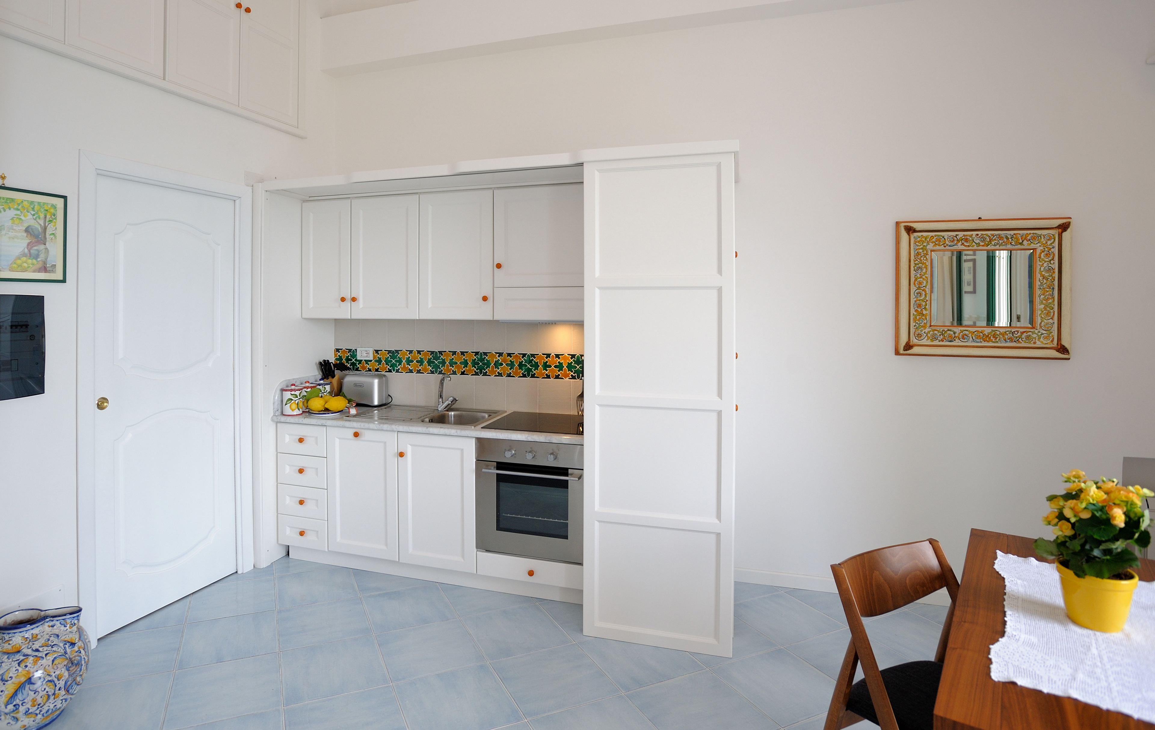 Una cocina con gabinetes blancos, un lavamanos de acero inoxidable y un salpicadero de azulejos.