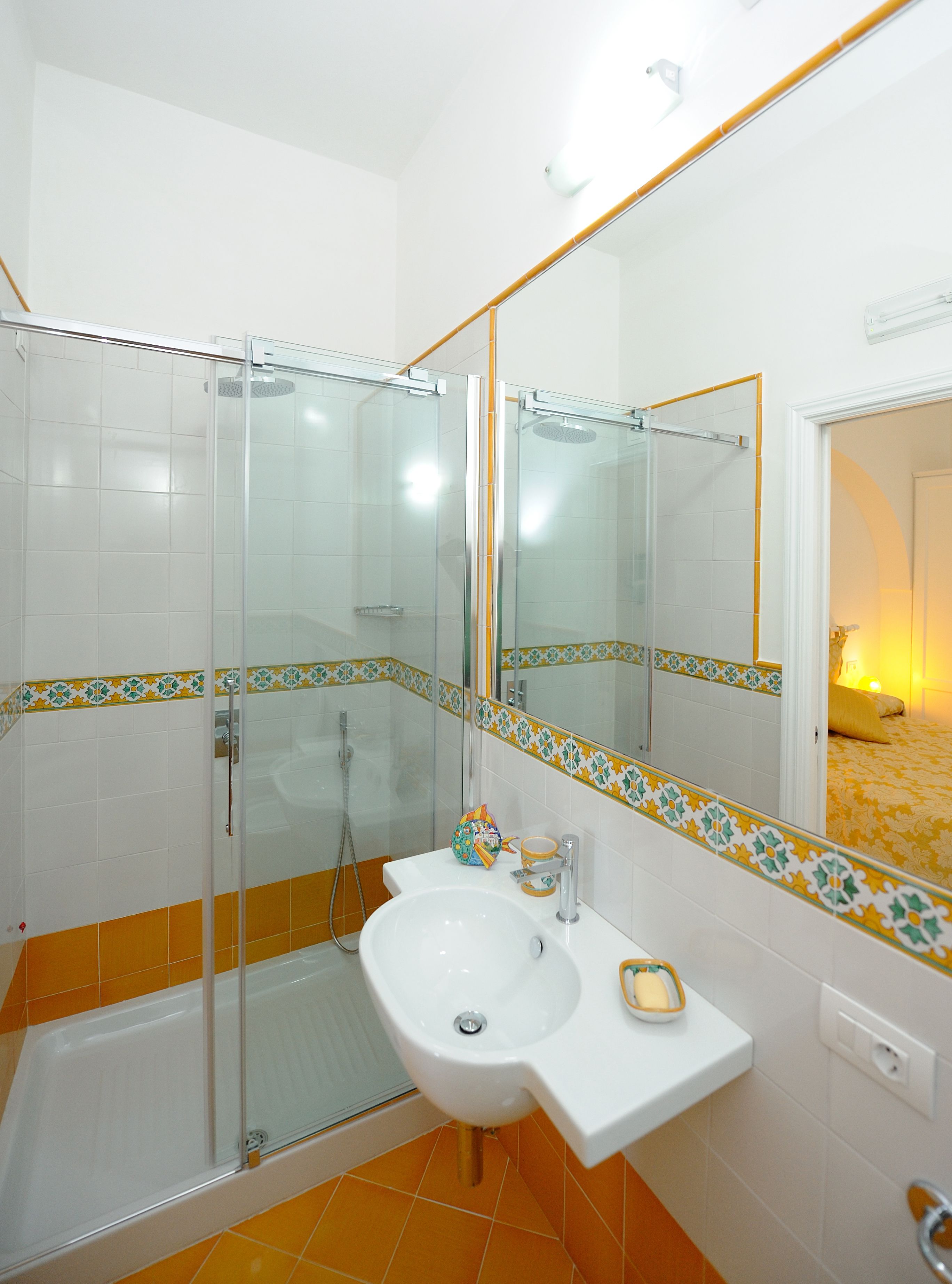 A bathroom with a glass shower enclosure, a white sink, and a mirror with a decorative tile border.
